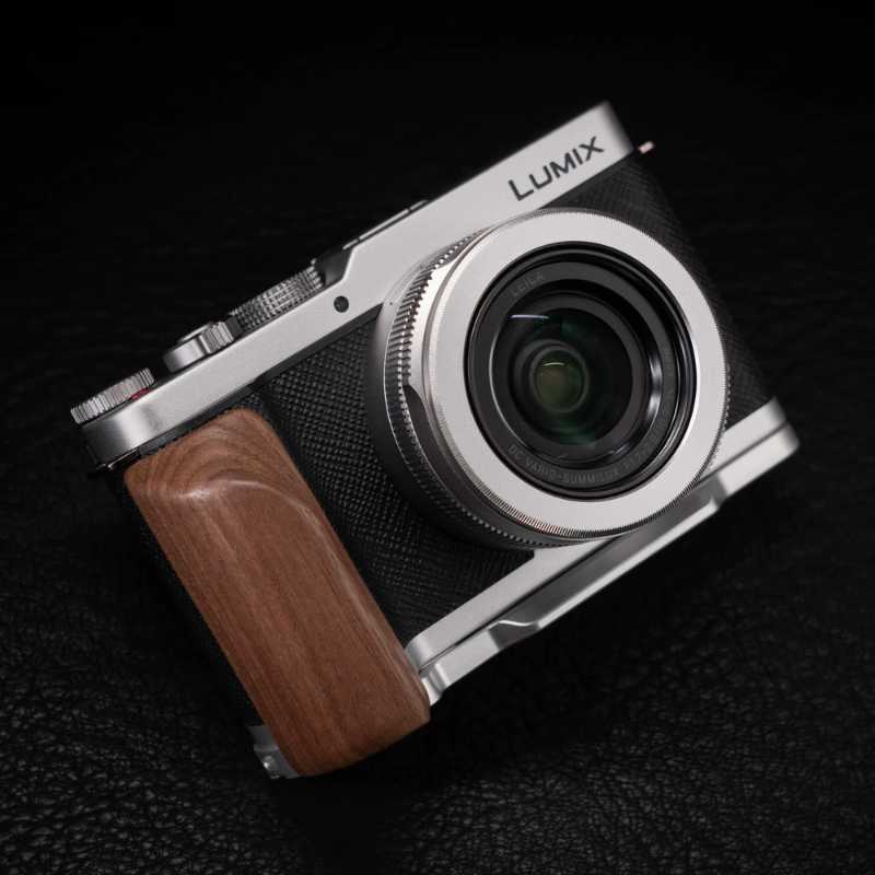 Panasonic Lumix compact camera with a silver metal body, black textured grip, and a brown wooden handgrip, shown on a dark textured background.