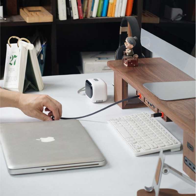 Wood Telescopic Retractable Data Cable Charging Cable For Desk iWoodStore Person plugging a cable into a laptop on a desk with a keyboard and other items.